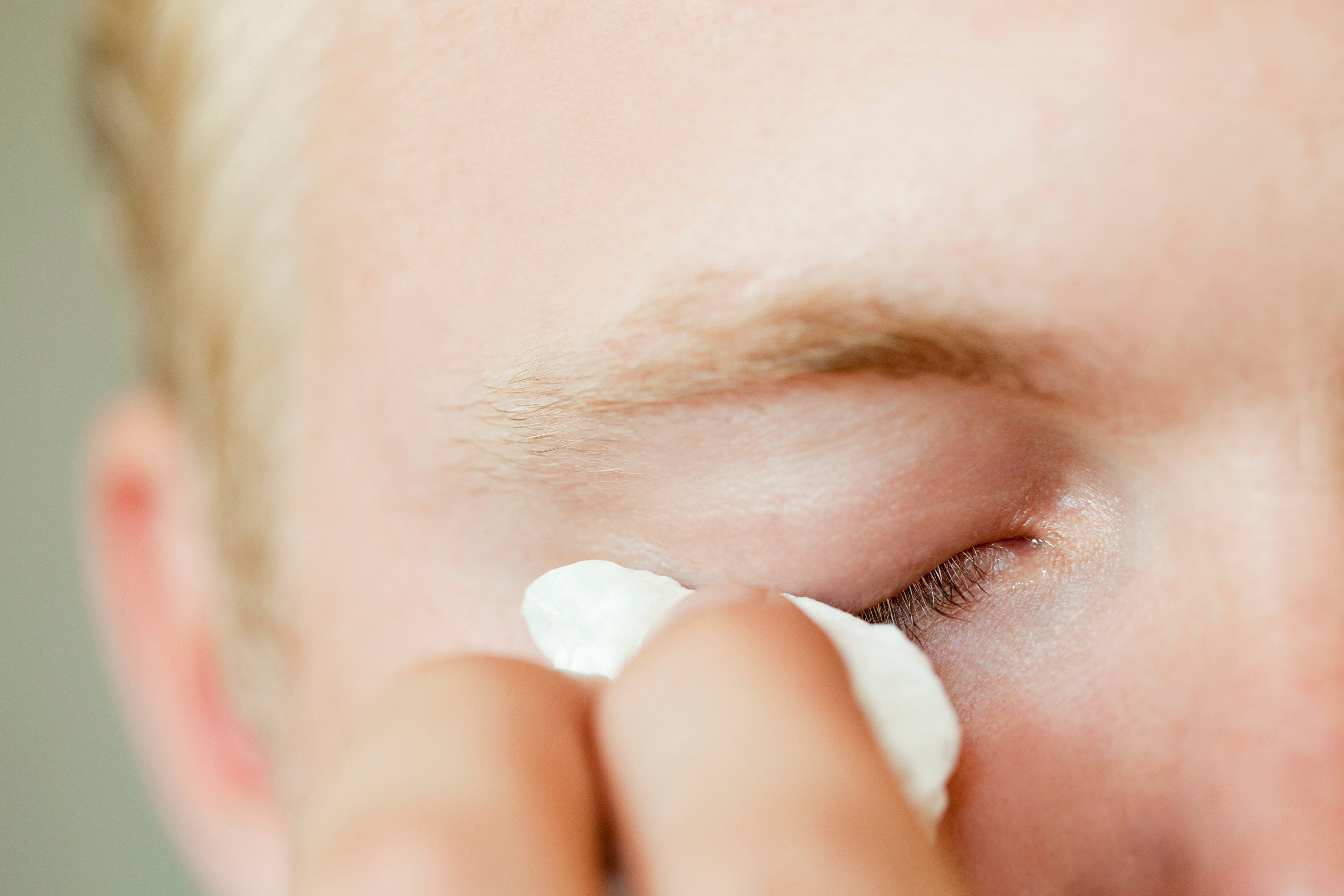man applying cream to eyelid