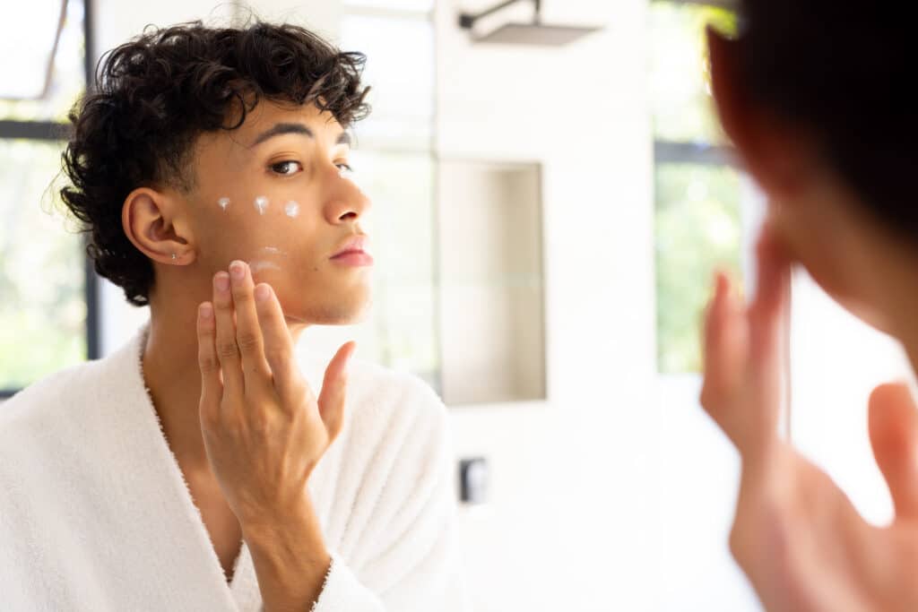 Teenage boy applying cream to sensitive skin on his face