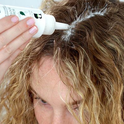 Woman applying Scalp Soothe to middle parting